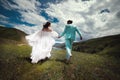 Rear view of running loving newlyweds holding hands, a bride in a wedding dress and a wife in a turquoise suit running Royalty Free Stock Photo