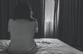 Rear view of sad and depressed woman take off glasses and sit on bed in hotel bedroom. Sad woman sit in dark bedroom. Girl with Royalty Free Stock Photo