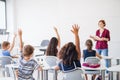 Rear view of school children sitting at the desk in classroom, raising hands. Royalty Free Stock Photo