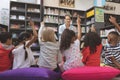 Rear view of school kids raising hand in library to answer at a question