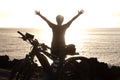 Rear view of senior active woman in front to the ocean at sunset. Black silhouette. Arms raised. Freedon and happiness concept.