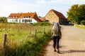 Rear view of senior adult woman walking on sidewalk parallel to rural road on outskirts of village Royalty Free Stock Photo