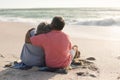 Rear view of senior biracial man sitting with arm around woman enjoying retirement at beach