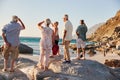 Rear View Of Senior Friends Standing On Rocks On Summer Group Vacation Looking Out To Sea