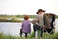 Rear view on senior man with grandson sitting near river with fishing rods in hands Royalty Free Stock Photo