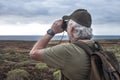 Rear view of senior man with white beard looking at the horizon with binoculars. Active retiree with backpack on shoulders