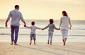 Rear view shot of a carefree family holding hands while walking on the beach at sunset. Mixed race parents and their two Royalty Free Stock Photo