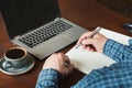 Rear view shot of hands busy business man writing by pen and using laptop at office desk. Royalty Free Stock Photo