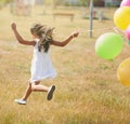 Happily hopping along. Rear view shot of a little girl running through a field with a string of balloons outside. Royalty Free Stock Photo