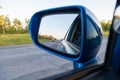 Rear view in the side mirror of a blue sedan with the reflection of heavy traffic on a country asphalt road on a summer day with Royalty Free Stock Photo