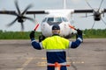 Rear view A signalman meets a passenger plane at the airport in front of propeller airplane. The plane is taxiing to the parking