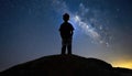 A silhouette of a boy on the edge of the world, looking at the starry sky at night. Generated with AI Royalty Free Stock Photo