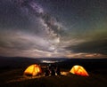 Rear view silhouette of four people sitting beside camp in night under sky with many stars Royalty Free Stock Photo