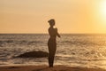 Rear view silhouette slim woman does yoga on tropical sea coast or ocean beach outdoors at sunset Royalty Free Stock Photo