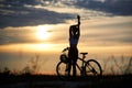 Rear view of silhouette sporty girl standing near bicycle against background evening sky