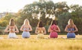 Rear view. Sitting in lotus pose with hands on the back. Group of women have fitness outdoors on the field together