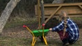 Rear view of a small girl playing with dirt in a park holding a toy wheelbarrow