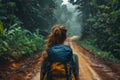 Rear view of a solo female traveler with a backpack walking on a muddy road in the misty rainforest, embarking on an adventure