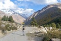 Rear View of Solo Indian traveler in winter clothing walking alone hiking a remote mountain road. Snow capped Himalayan mountain