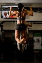 Rear view of strong muscular body of woman doing pull ups in gym.