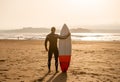 Rear view of strong surfer with surfboard on the beach at sunset or sunrise. Silhouette of surf man standing looking at ocean