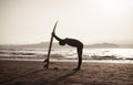 Rear view of strong surfer with surfboard on the beach at sunset or sunrise. Silhouette of surf man standing looking at ocean