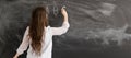 Rear view of a student or teacher with long brunette hair writing on a blank chalk board or blackboard with copyspace Royalty Free Stock Photo