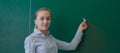 Rear view of a student or teacher with long brunette hair writing on a blank green blackboard or chalkboard with copyspace Royalty Free Stock Photo