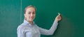 Rear view of a student or teacher with long brunette hair writing on a blank green blackboard or chalkboard with copyspace Royalty Free Stock Photo