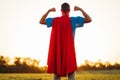 Rear view, Successful hero wears red mask and cape, raises arms, shows biceps, shows courage and strength