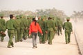 Rear view, Teen girl in red shirt walking with a group of Young Vietnamese soldier on the street, during site visit program. Dien