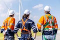 Rear view of three caucasian engineers in uniform and hardhat talk about system installation at agricultural field with wind