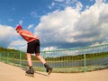 Rear view to inline skater in red t-shirt and black pants skating on the bridge . Outdoor inline skating