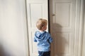 A rear view of toddler boy standing near door inside in a bedroom.