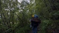 Rear view of travelers with backpacks walking on forest trail. Stock footage. Travelers follow each other along narrow