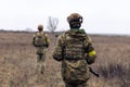 Rear view of two armed Ukrainian soldiers walking in steppe in uniform and helmets