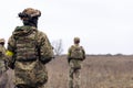 Rear view of two armed Ukrainian soldiers walking in steppe in uniform and helmets