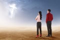 Rear view of two asian business people standing on desert and looking at glowing christian cross