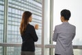 two asian businesswomen standing talking chatting by the window in office