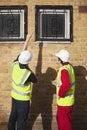 Rear view of two male workers in hardhats pointing towards windows