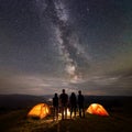 Rear view two young couples at night in tent camp stand enjoying starry sky, Milky way, mountains and luminous town Royalty Free Stock Photo