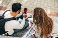 Rear view of two young students looking to the mobile phone sitting on the stairs of the college campus outdoors. A young woman Royalty Free Stock Photo