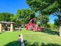Rear view unidentified kids walking, running at firetruck themed playground with green artificial grass turf carpet, tall trees
