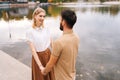 Rear view of unrecognizable bearded man talking with charming blonde woman standing outdoors by beautiful lake at city Royalty Free Stock Photo