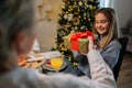 Rear view of unrecognizable loving grandmother giving festive box with Christmas present to adorable granddaughter Royalty Free Stock Photo