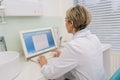 Rear view of unrecognizable middle-aged woman general practitioner in white coat using laptop computer writing notes at Royalty Free Stock Photo