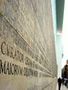 Rear view of an unrecognizable person walking along a wall with Latin epigraph, Rome, Italy