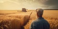 Rear view of an upper part of old man standing in the wheat filed. Adult farmer looking at combine cutting the dry crop. Royalty Free Stock Photo