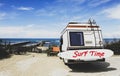 Rear view of vintage camper parked on the  beach against a beautiful scenic view - Caravan of surfer with a surfboard on back - Royalty Free Stock Photo