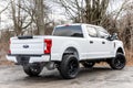 Rear view of a white 2020 Ford F-250 pickup truck with lifted wheels on a dirt road